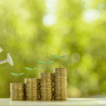 Mano regando con una regadera pilas de monedas con plantas creciendo, representando cómo la inversión de impacto fomenta el crecimiento financiero y ambiental en un fondo verde desenfocado.